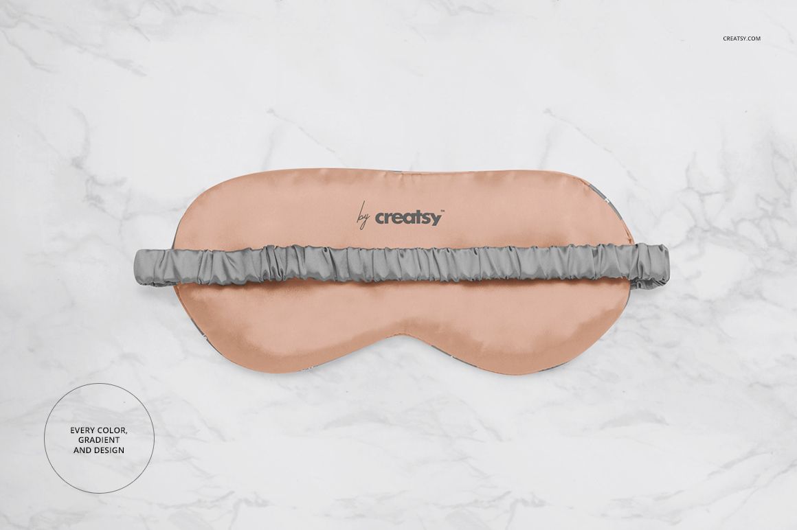 Eye mask mockup featuring a soft peach fabric and gray elastic band, laid flat on a marble surface.