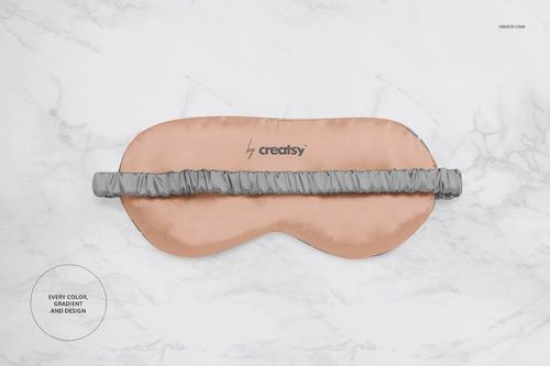 Eye mask mockup featuring a soft peach fabric and gray elastic band, laid flat on a marble surface.