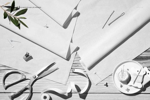 Flat lay of two light-colored cotton fabrics mockup on a table, with scissors, pins, and sewing supplies nearby.