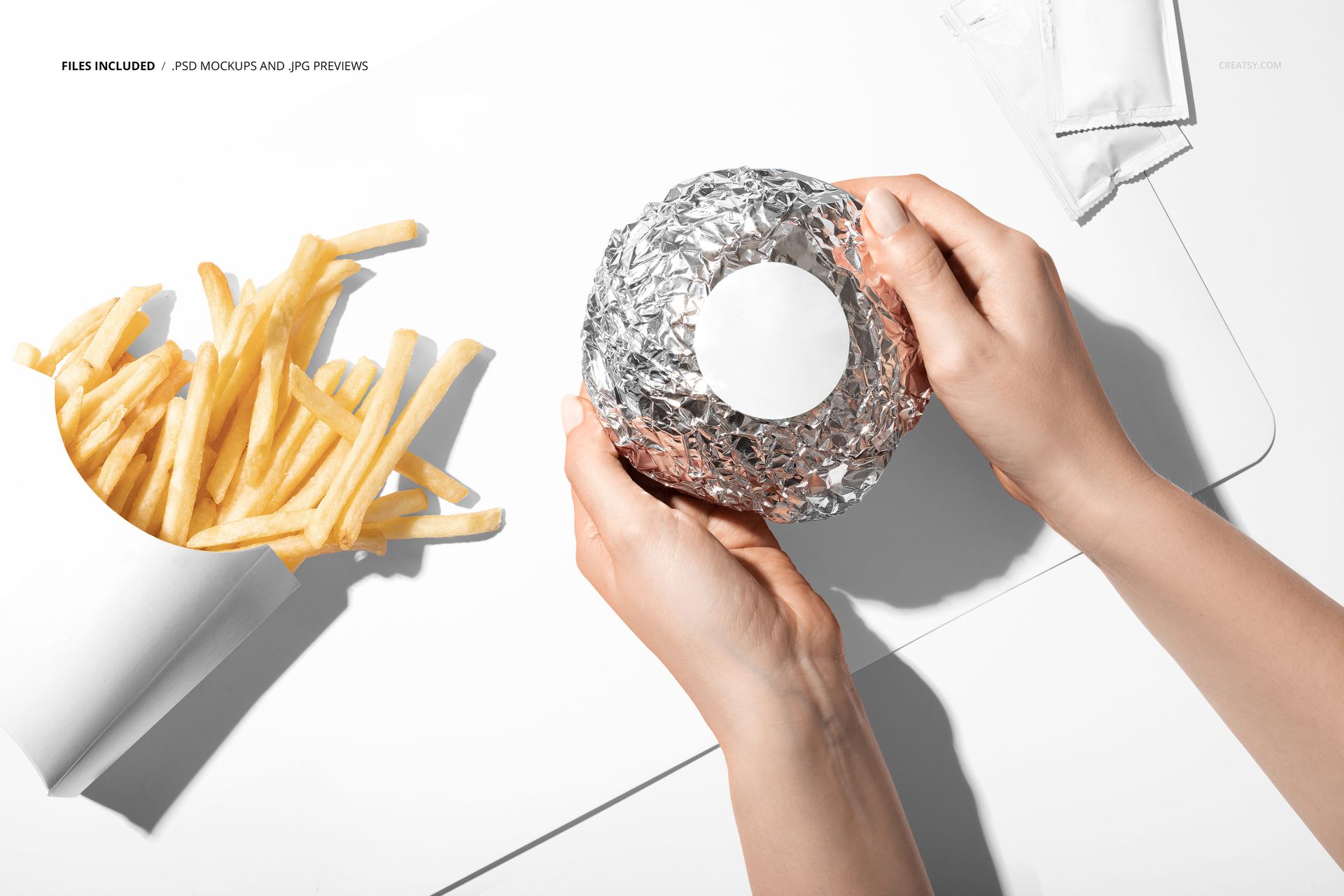 PSD mockup showing a foil-wrapped burger and french fries arranged on a minimalist white placemat with napkins nearby.
