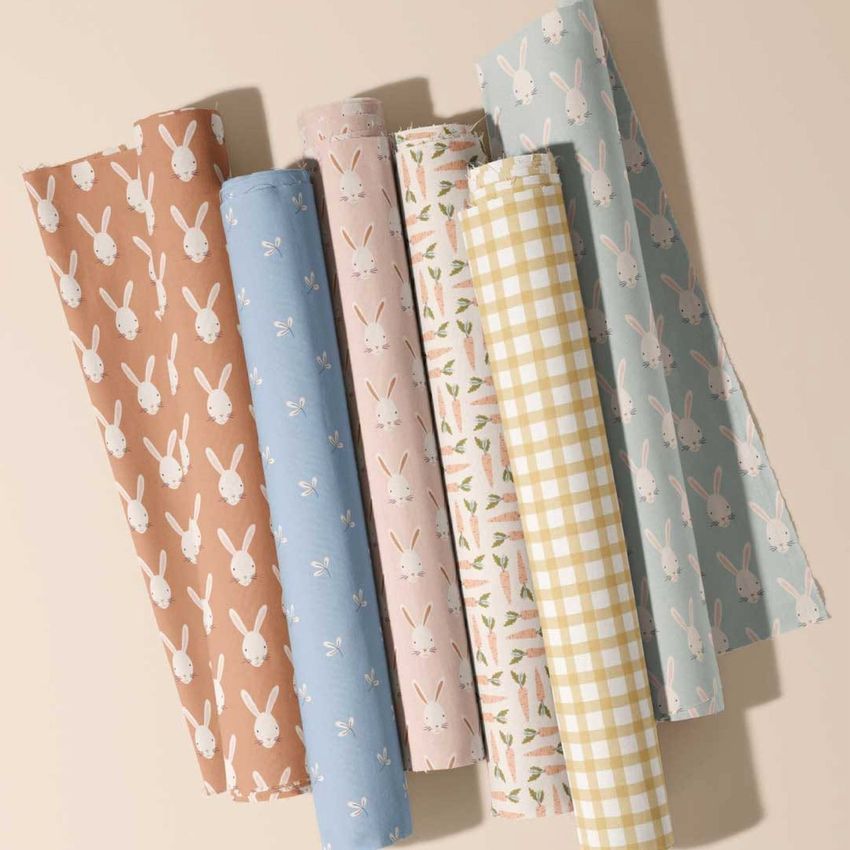 Fabric rolls mockup featuring six rolls with pastel patterns, including bunnies, carrots, florals, and gingham on a beige surface.