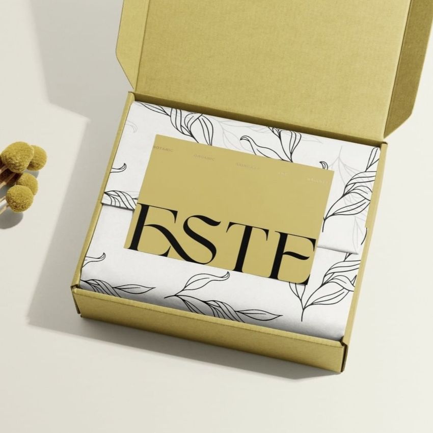 Stationery card mockup featuring a gold card with bold black text placed inside an open kraft box with floral tissue paper.