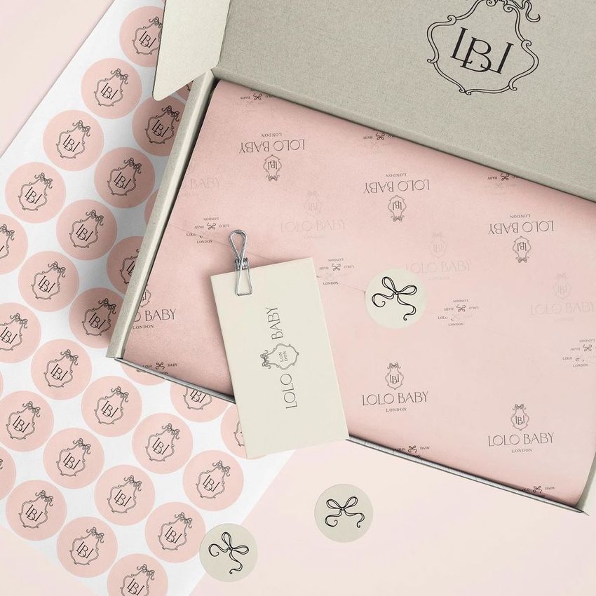 Mailing box mockup featuring a pink box with custom logo tissue paper, a branded tag, and round stickers on a neutral background.