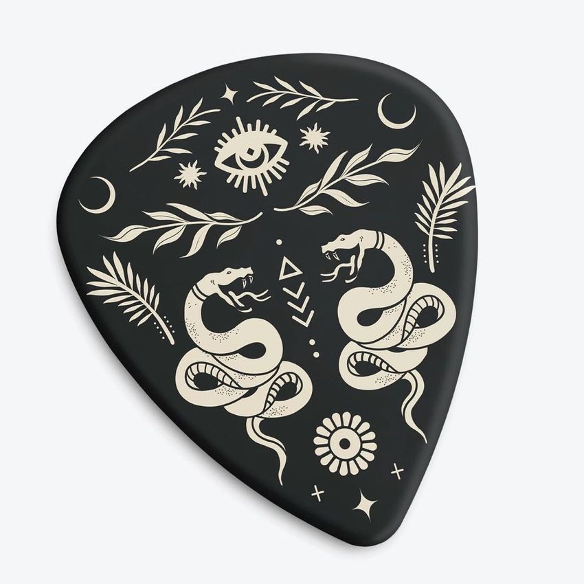 Guitar pick mockup featuring a black pick with beige tattoo-style designs of snakes, leaves, an eye, and geometric shapes on a plain background.