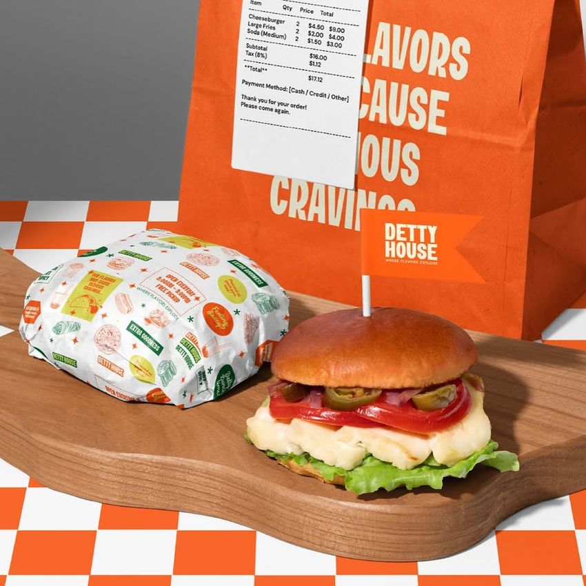 Burger packaging mockup featuring a wrapped sandwich, an unwrapped burger on a wooden board, and an orange paper bag in the background.
