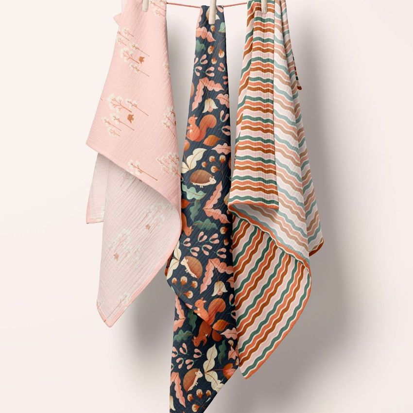 A set of three swaddle blanket mockups with floral, striped, and wavy designs displayed on a hanging rod.