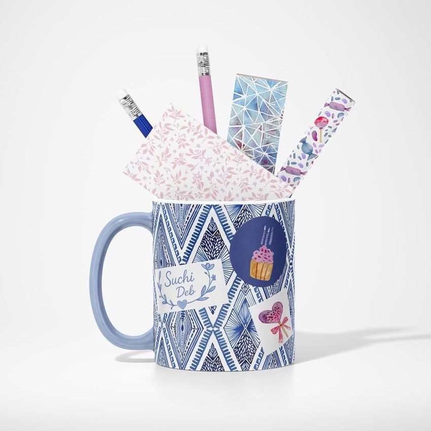 Mug mockup with a blue geometric diamond pattern, filled with pencils, pens, and patterned stationery on a light background.