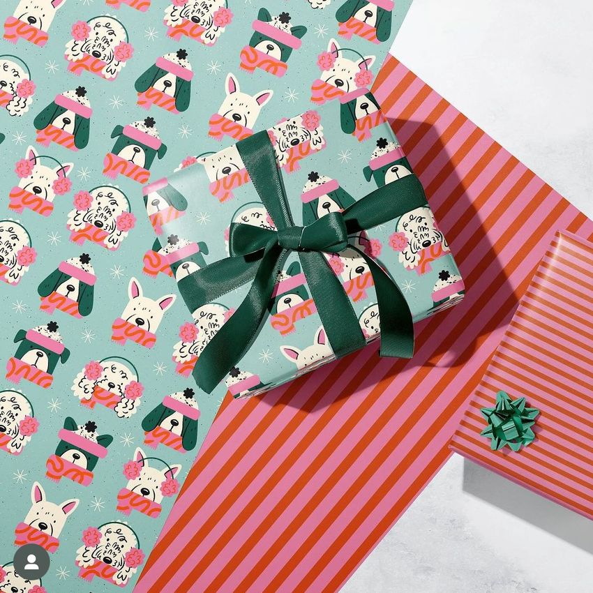Wrapping paper mockup featuring a gift box wrapped in teal paper with cartoon dog faces in winter hats, surrounded by matching sheets and striped designs.