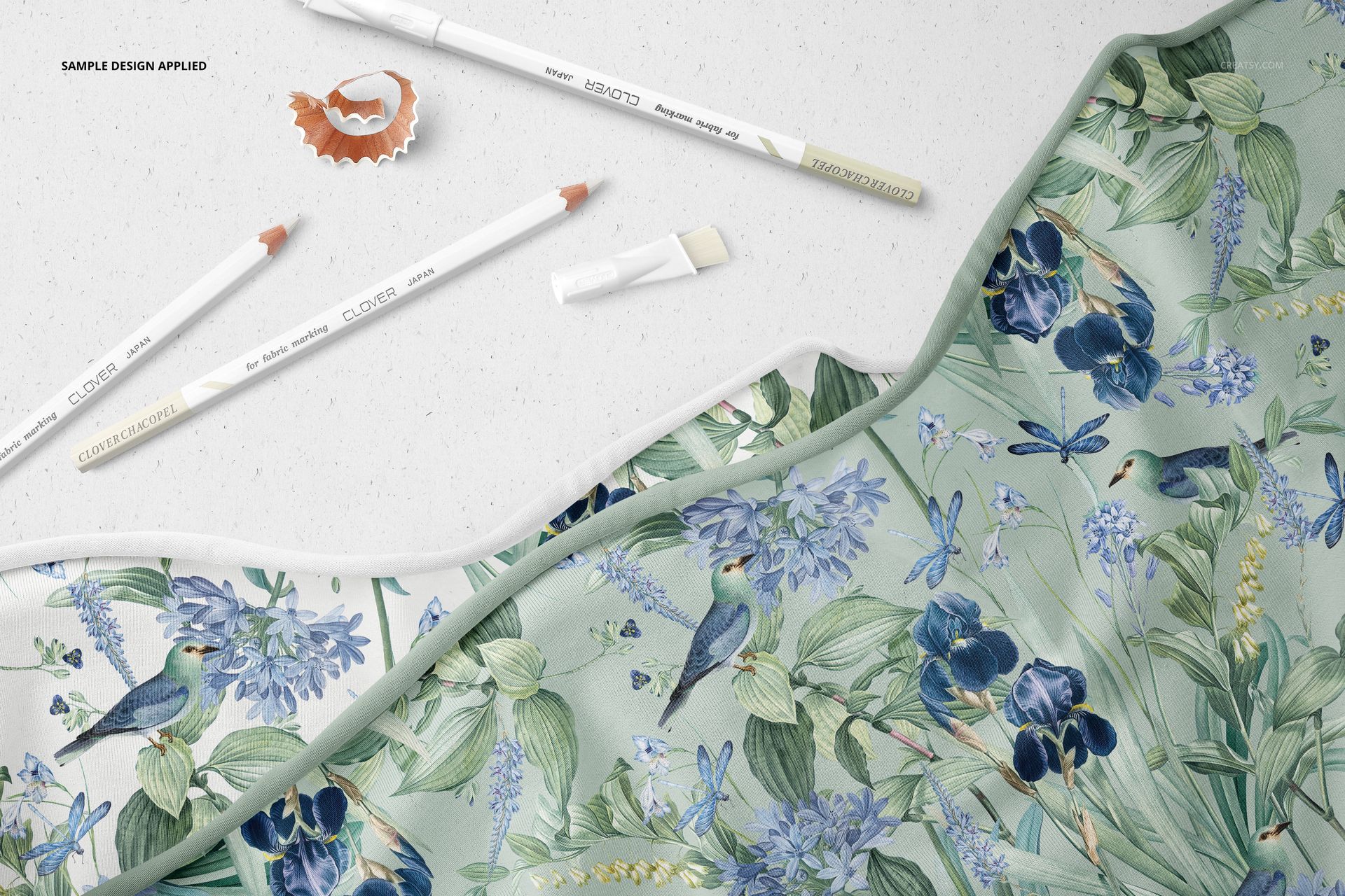 Botanical-themed jersey fabric mockup shown from a top view, with marking pencils and a pencil shaving nearby.
