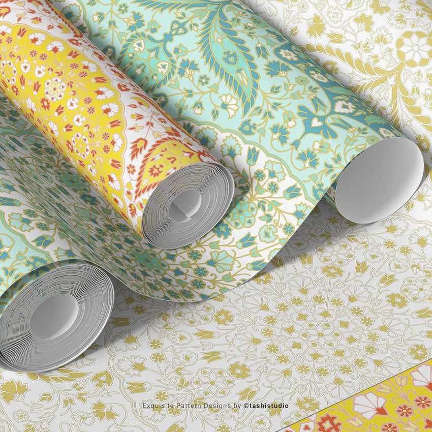 Paper wallpaper mockup featuring several rolled sheets with intricate floral and botanical patterns in yellow, teal, and gold tones.