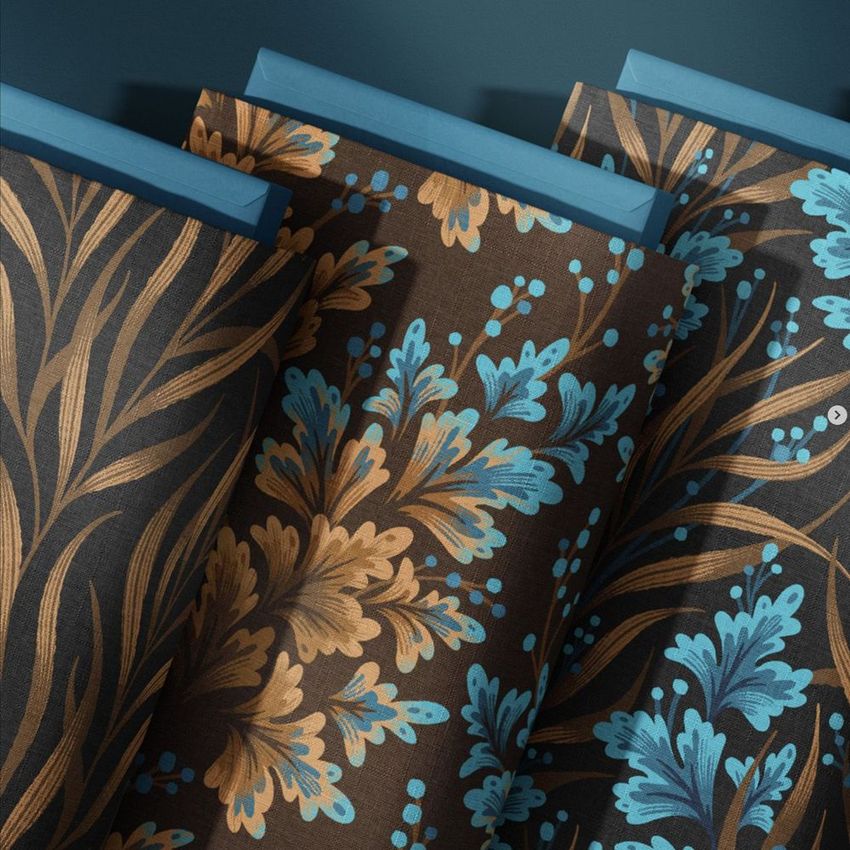Fabric bolts mockup featuring three rolls of cloth with blue and gold botanical patterns on a dark background, viewed from above.