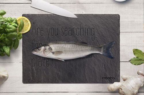 Slate plate mockup featuring a whole fish placed on a dark rectangular slate, viewed from above on a light wooden surface.