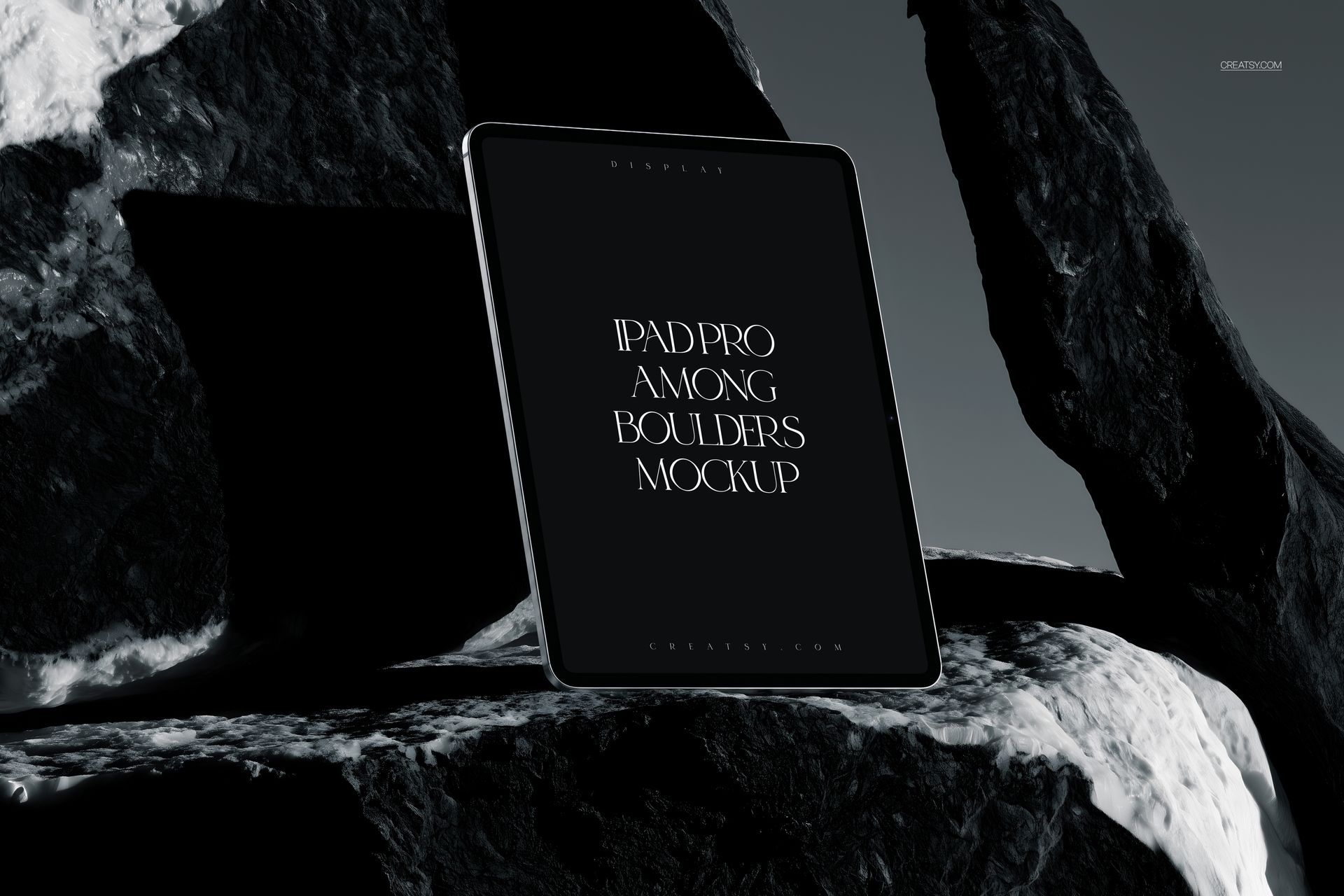 Front view of iPad Pro mockup standing against dark rocky boulders, featuring a minimalist black display.