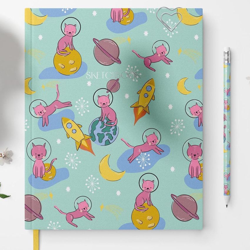 Stationery mockup featuring a notebook with a mint green cover decorated with illustrated cats in space helmets, planets, and rockets.