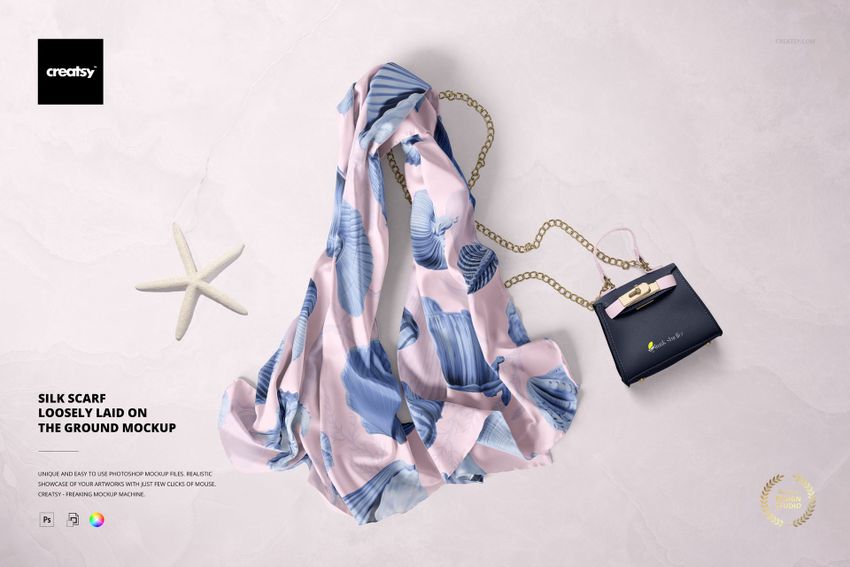 PSD mockup showing a chiffon silk scarf with soft pastel leaf motifs, arranged on a pale textured background with props.