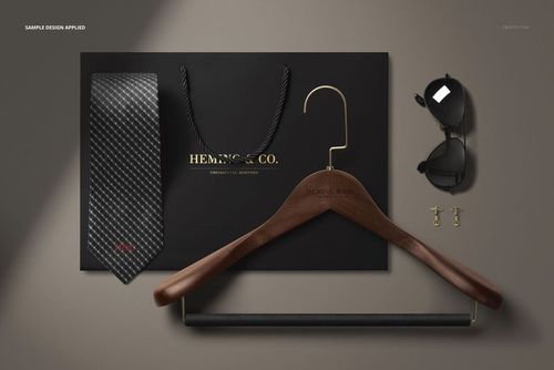 Flat lay of men’s accessories mockup featuring a black tie, hanger, sunglasses, cufflinks, and a black paper bag.