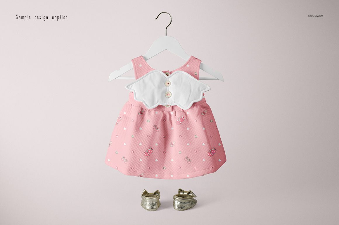 Pink baby dress mockup with white collar and decorative buttons, shown on a hanger with metallic baby shoes below.