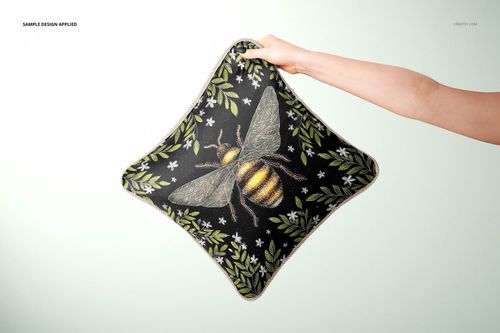 Front view of a square silk cushion mockup with braid trim, decorated with a bee and green leafy floral design.