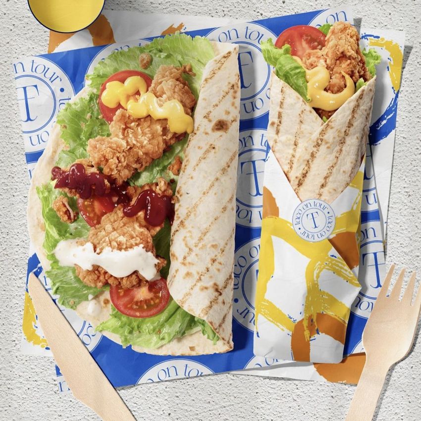 Food safe paper mockup showing a tortilla wrap and an open flatbread with fried chicken, lettuce, tomato, and sauces on colorful printed wrappers.