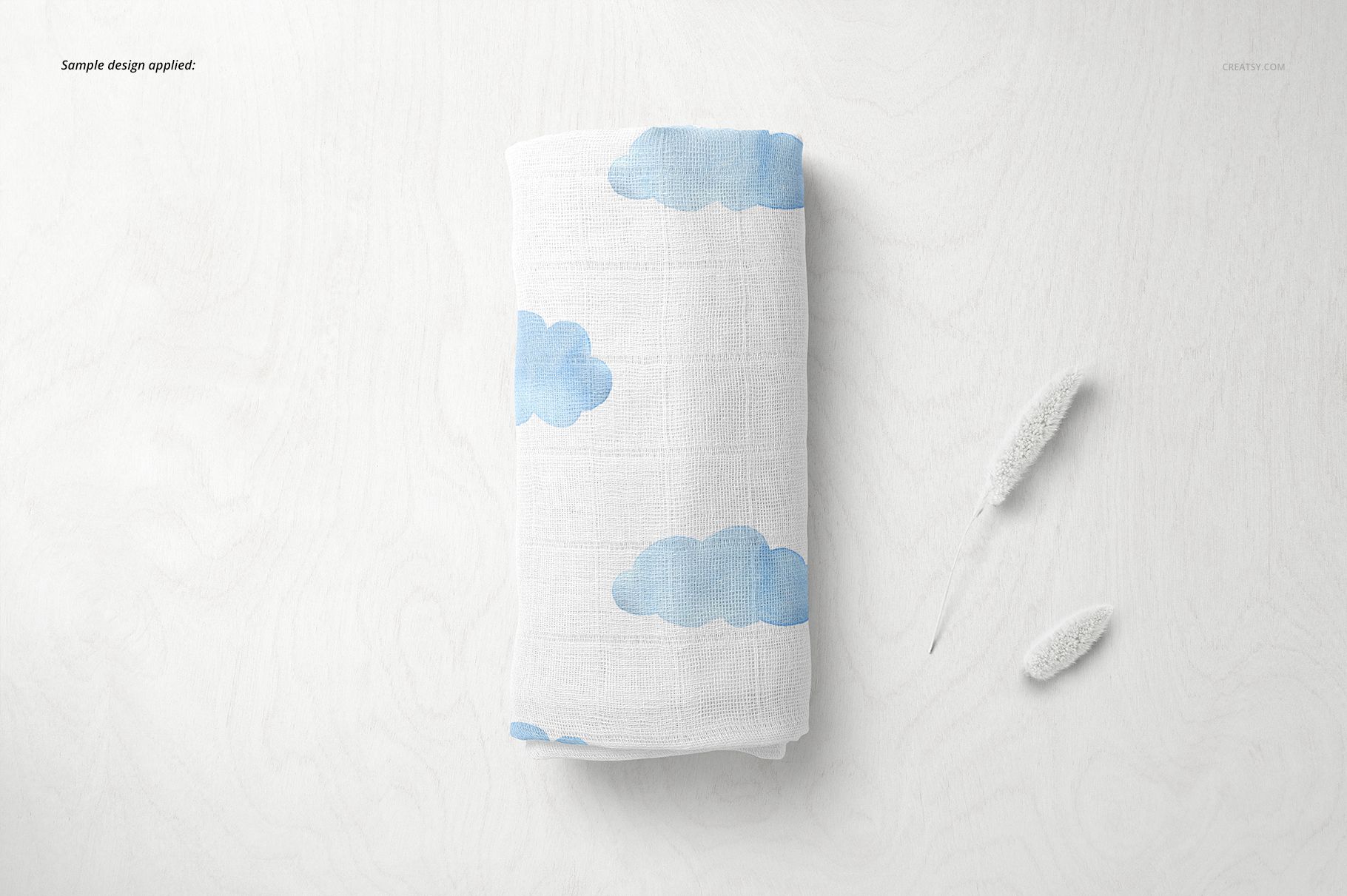 Baby muslin nappy mockup featuring a white cloth with blue clouds, displayed from above on a pale wood background.