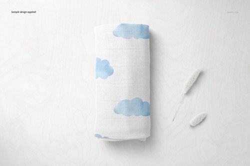 Baby muslin nappy mockup featuring a white cloth with blue clouds, displayed from above on a pale wood background.