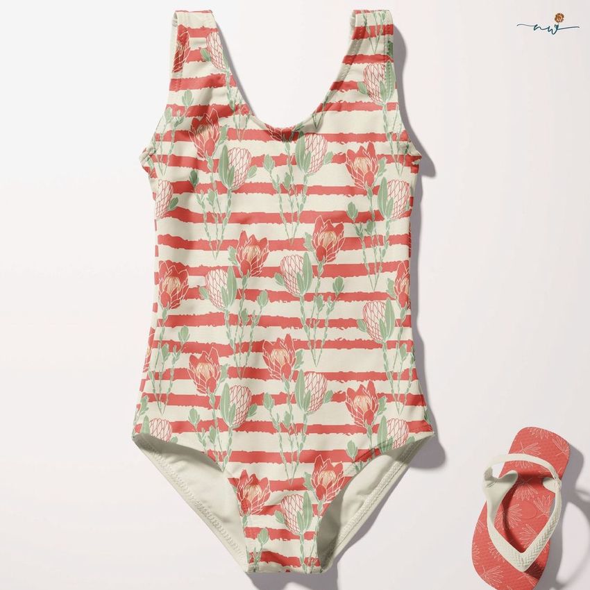 Baby swimsuit mockup featuring a sleeveless one-piece with a pink protea floral and striped pattern, shown flat on a light surface with matching sandals.