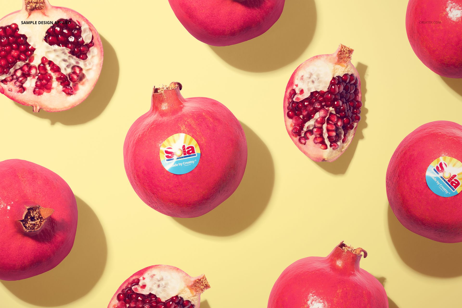 Round fruit stickers displayed on whole and halved pomegranates, arranged on a light yellow surface in a mockup scene.