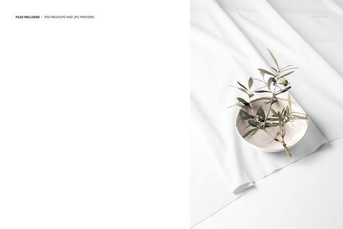 Cotton fabric mockup featuring a white cloth with soft folds, a ceramic bowl, and an olive branch from a top view.