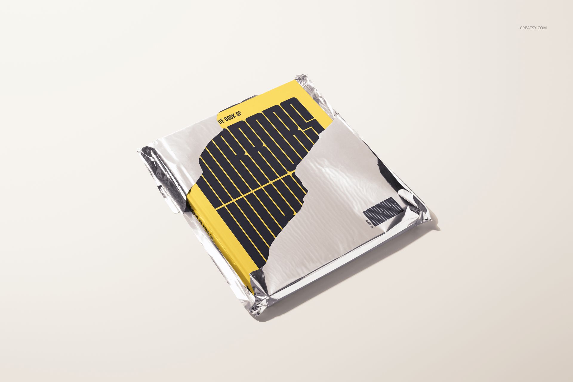 Mockup of a hardcover book in yellow and black, with crinkled metallic foil wrapping, displayed on a pale background.