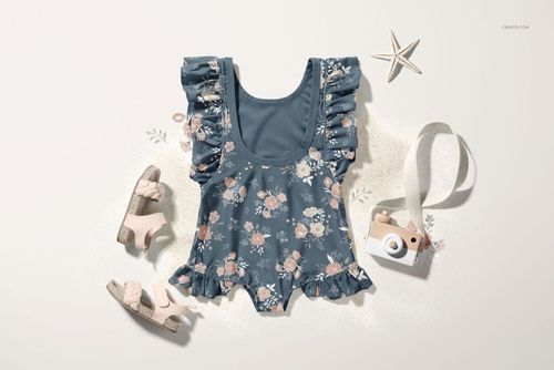 Front view of a baby ruffle swimsuit mockup with blue floral pattern, surrounded by sandals, a toy camera, and a starfish.
