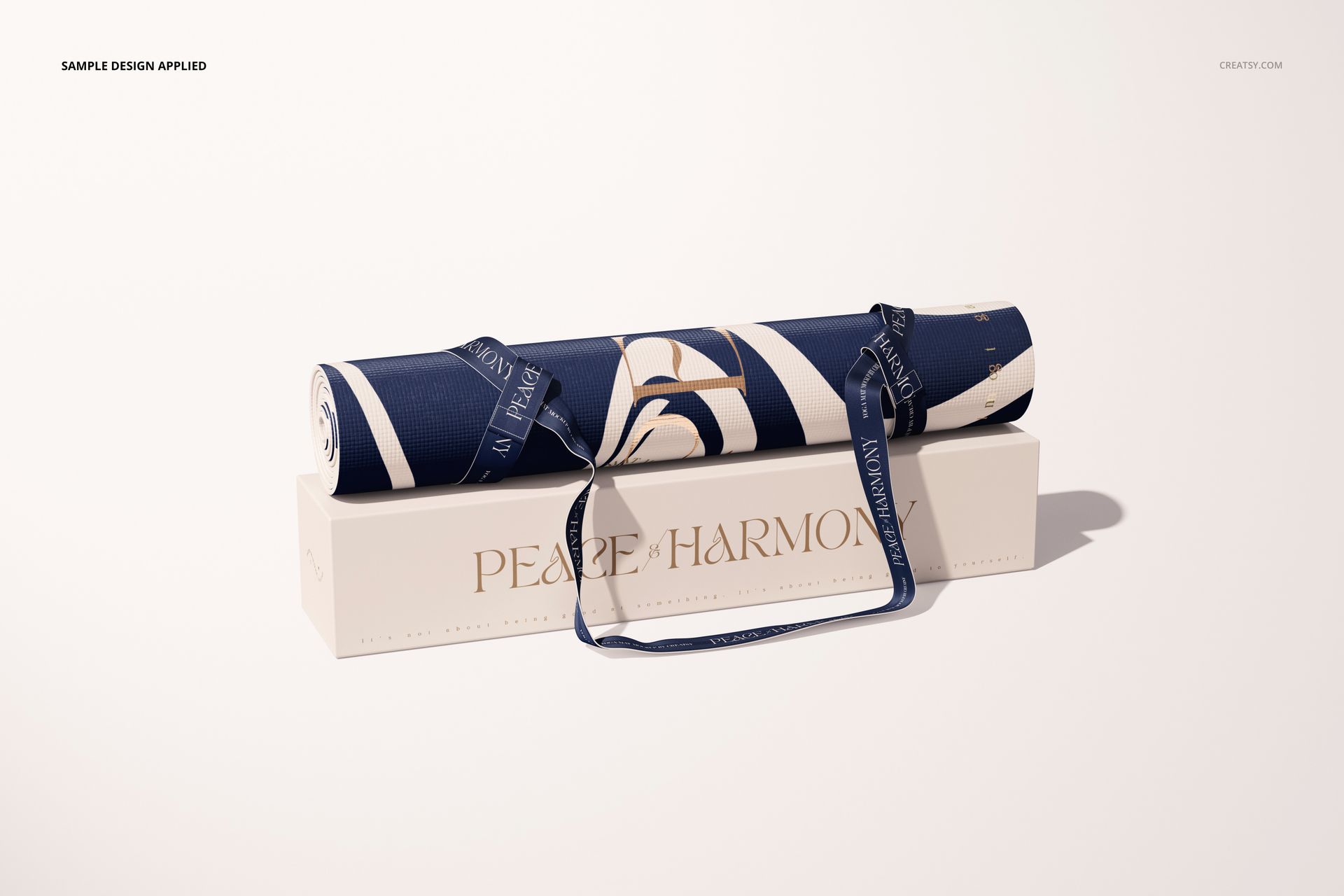Yoga mat mockup featuring a rolled mat with navy and beige design, displayed atop a rectangular box and strap.
