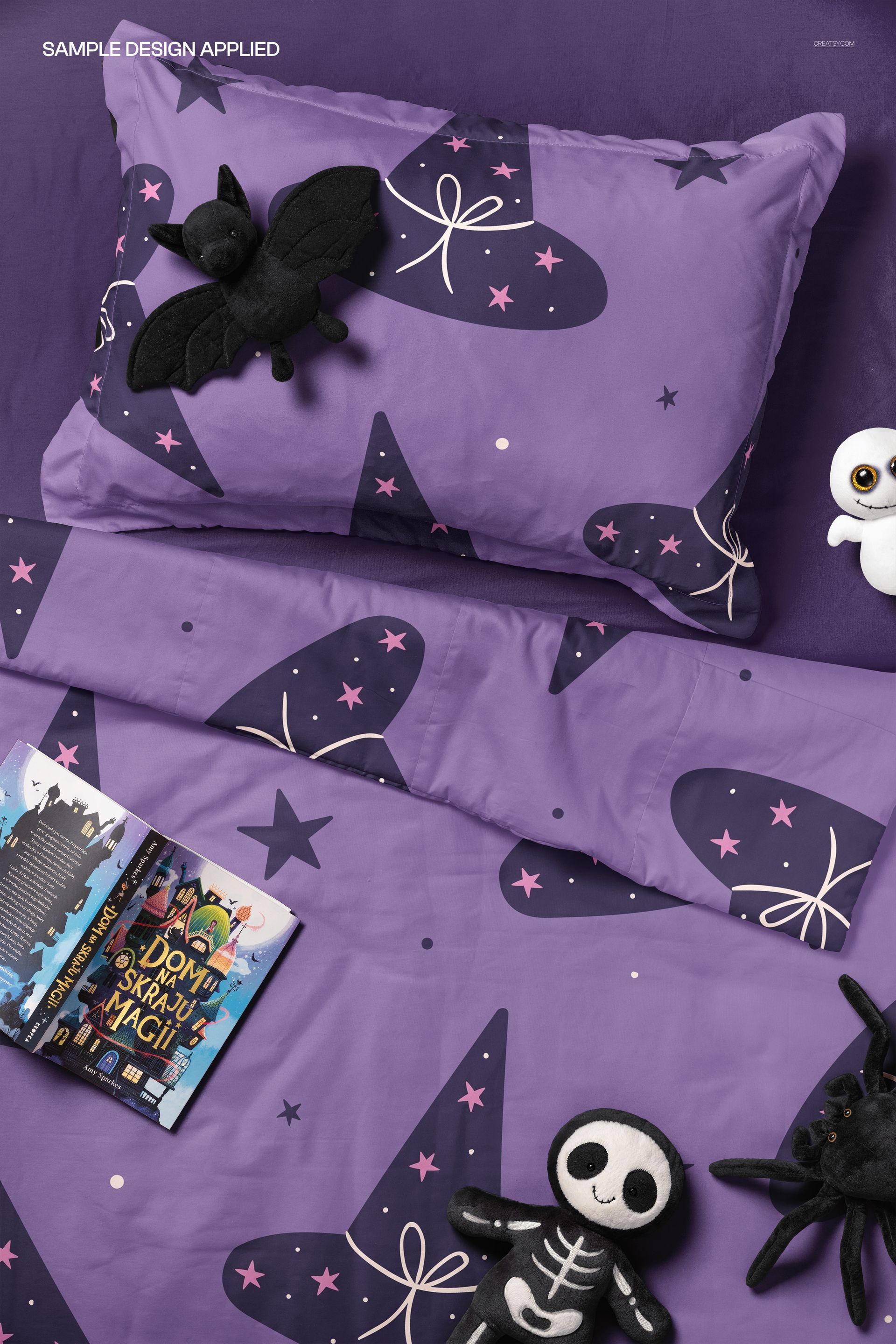 Children’s bedding mockup with purple pillow and duvet decorated with witch hats, plush bat, skeleton, and spider toys.