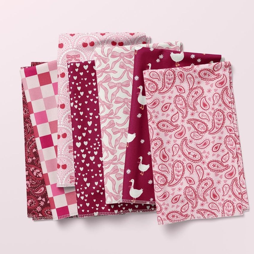 Folded fabrics mockup showing six pieces of fabric in pink and burgundy tones with various patterns on a light background.