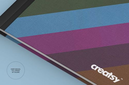 Fabric notebook mockup with diagonal stripes in green, blue, purple, and brown on a light blue surface, front view.