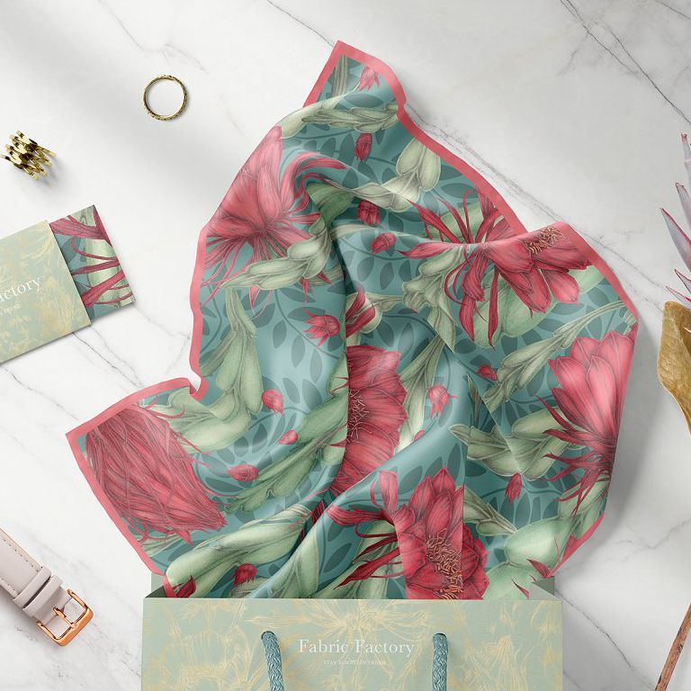 Silk scarf mockup featuring a folded scarf with a red and green floral pattern, displayed on a marble surface next to a shopping bag.