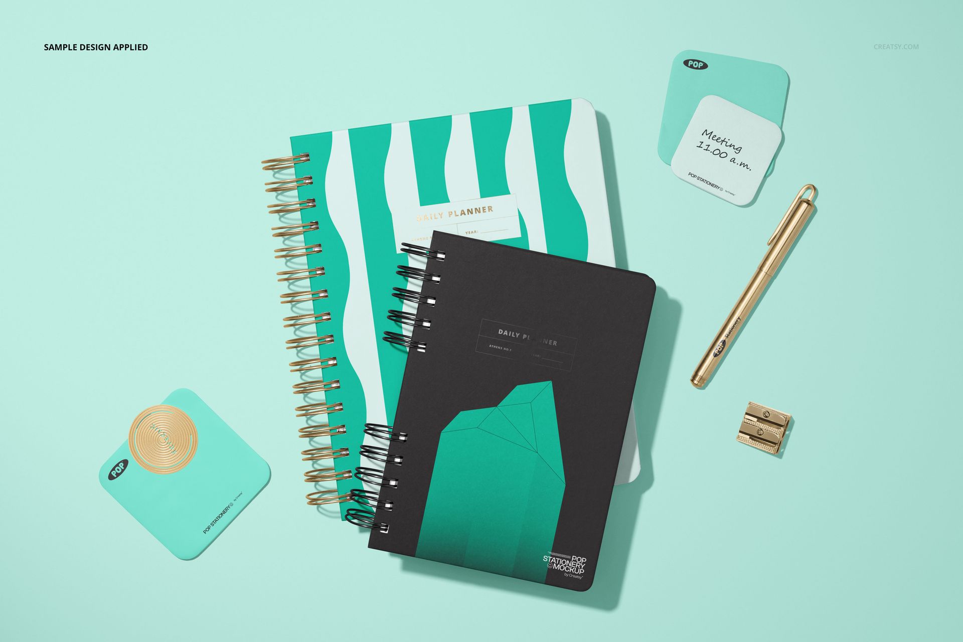 Stationery mockup featuring two spiral planners, sticky notes, a gold pen, and a sharpener arranged on a light mint surface.