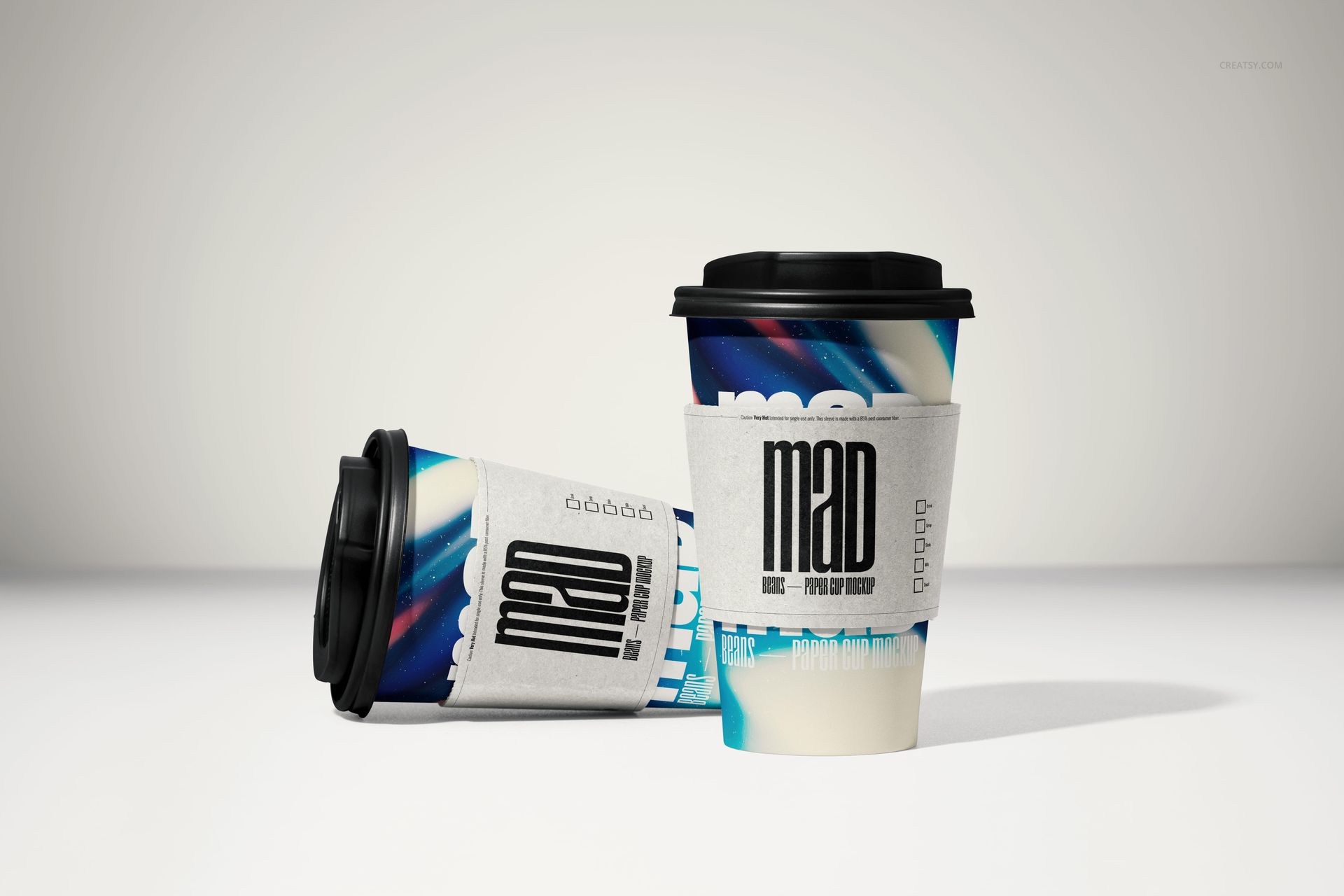 PSD mockup of paper cups with black lids, white sleeves, and bold blue and red patterns, displayed on a plain surface.