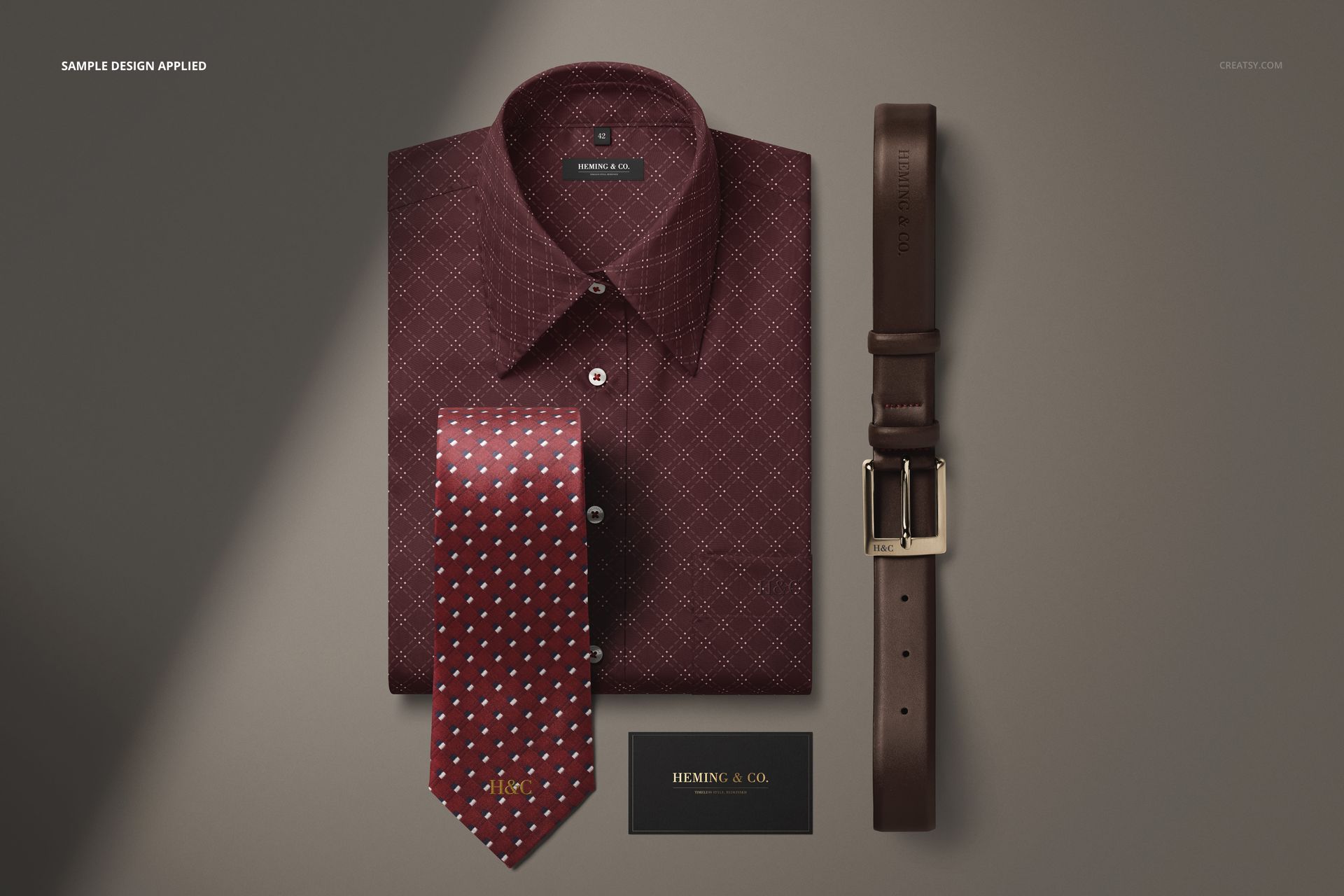 Folded men’s dress shirt in dark red with geometric pattern, paired with a polka dot tie, leather belt, and business card mockup.