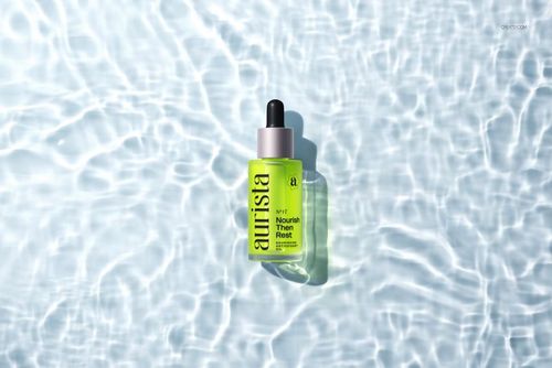 Green dropper bottle mockup with black top, placed on rippling water surface, top-down perspective.