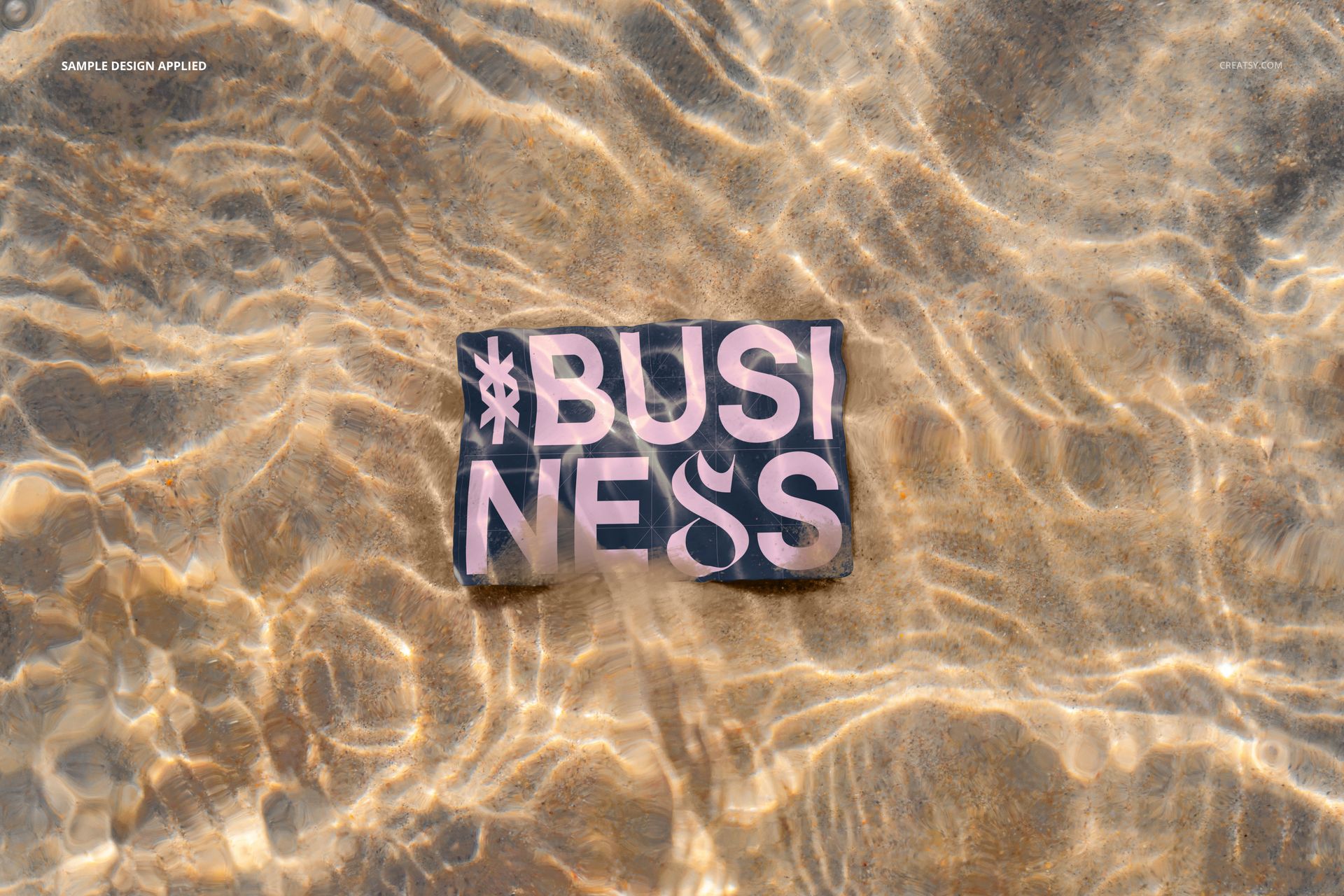 Business card mockup lying on sandy beach underwater, showing bold text design with sunlight reflections.