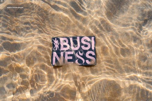 Business card mockup lying on sandy beach underwater, showing bold text design with sunlight reflections.