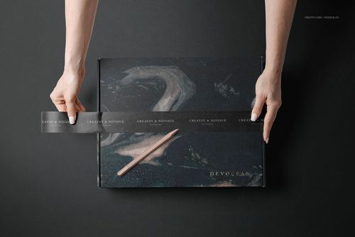 Mockup of a mailing box featuring swirling dark colors, hands sealing it with clear tape, shown on a black background.