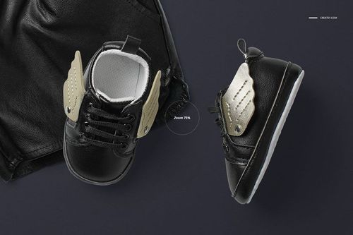 PSD mockup showing black infant shoes with metallic gold wings, arranged next to dark clothing on a solid background.