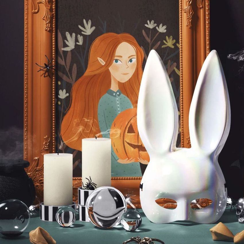 Halloween art print mockup featuring an ornate picture frame with an illustrated red-haired elf, surrounded by candles, a white rabbit mask, and glass spheres on a teal surface.