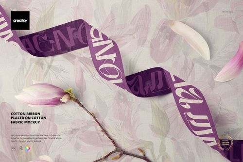 Purple cotton ribbon with white abstract design placed on light cotton fabric, viewed from above with magnolia flowers.