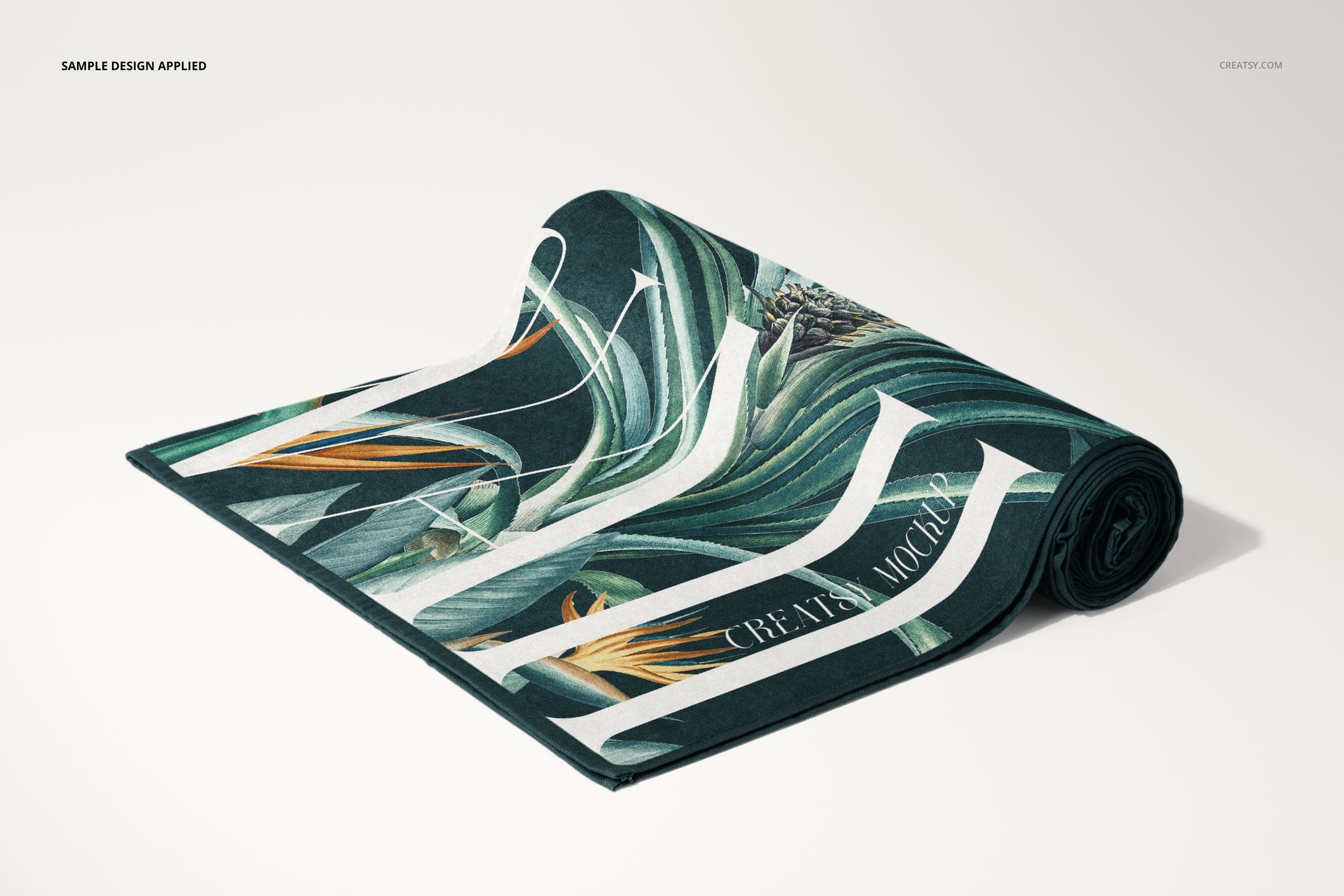 Rolled beach towel mockup with a tropical leaf pattern in green, orange, and white, displayed on a plain surface.