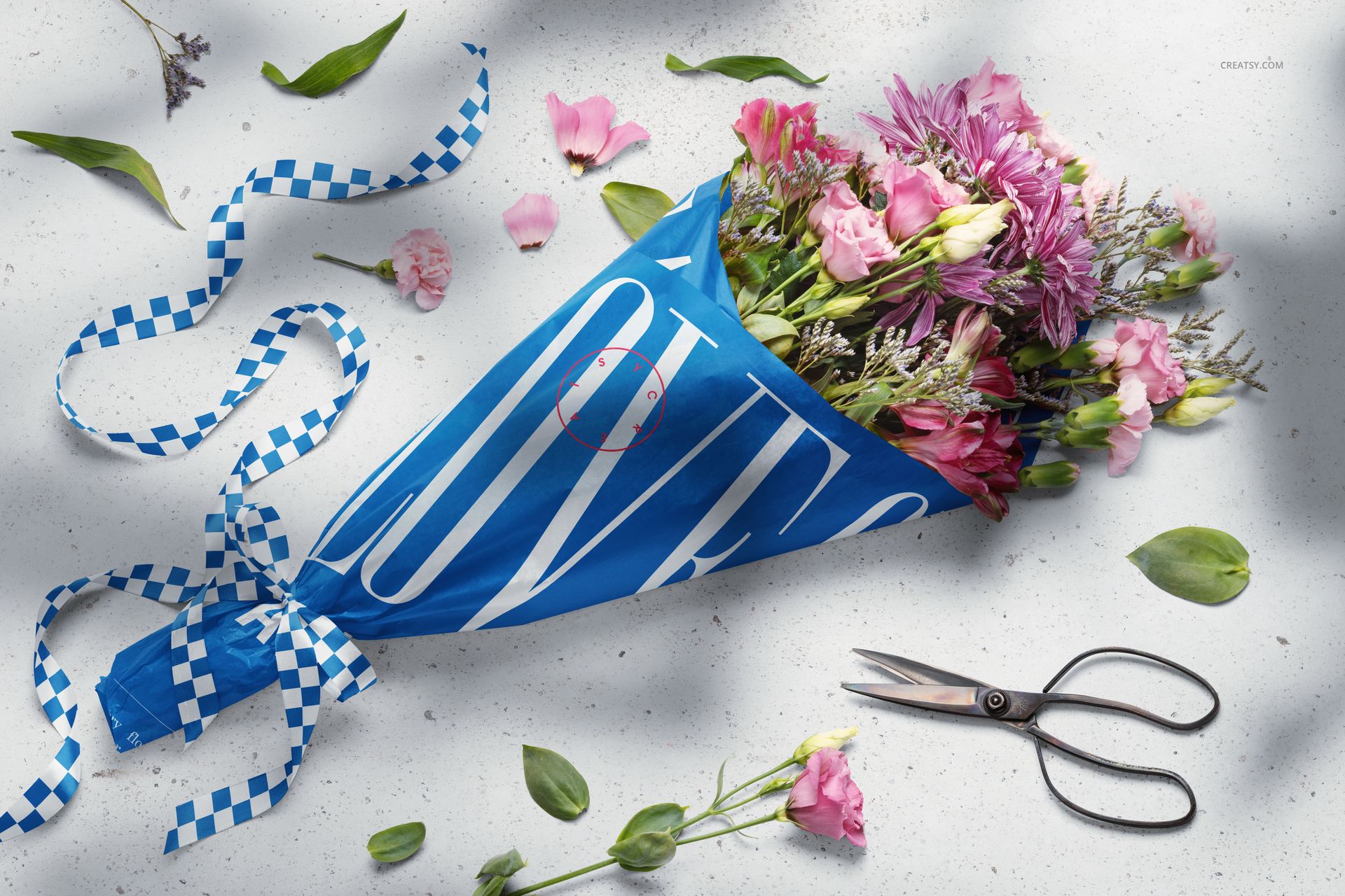 PSD mockup showing a vibrant floral bouquet in blue wrapping paper, with loose petals, ribbon, and scissors arranged around it.
