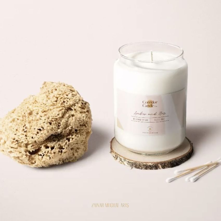 Packaging mockup showing a white candle in a jar with a sticker, styled with a sponge and swabs on a neutral tabletop.