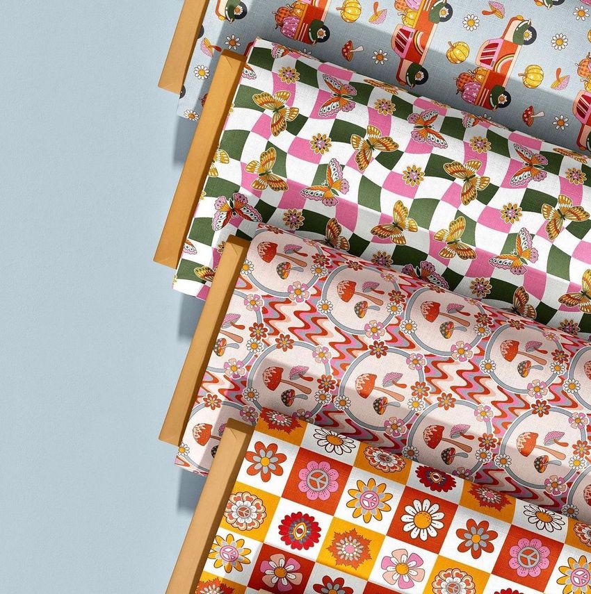 Fabric bolts mockup showing four rolled fabrics with colorful retro patterns, arranged diagonally on a light blue surface.