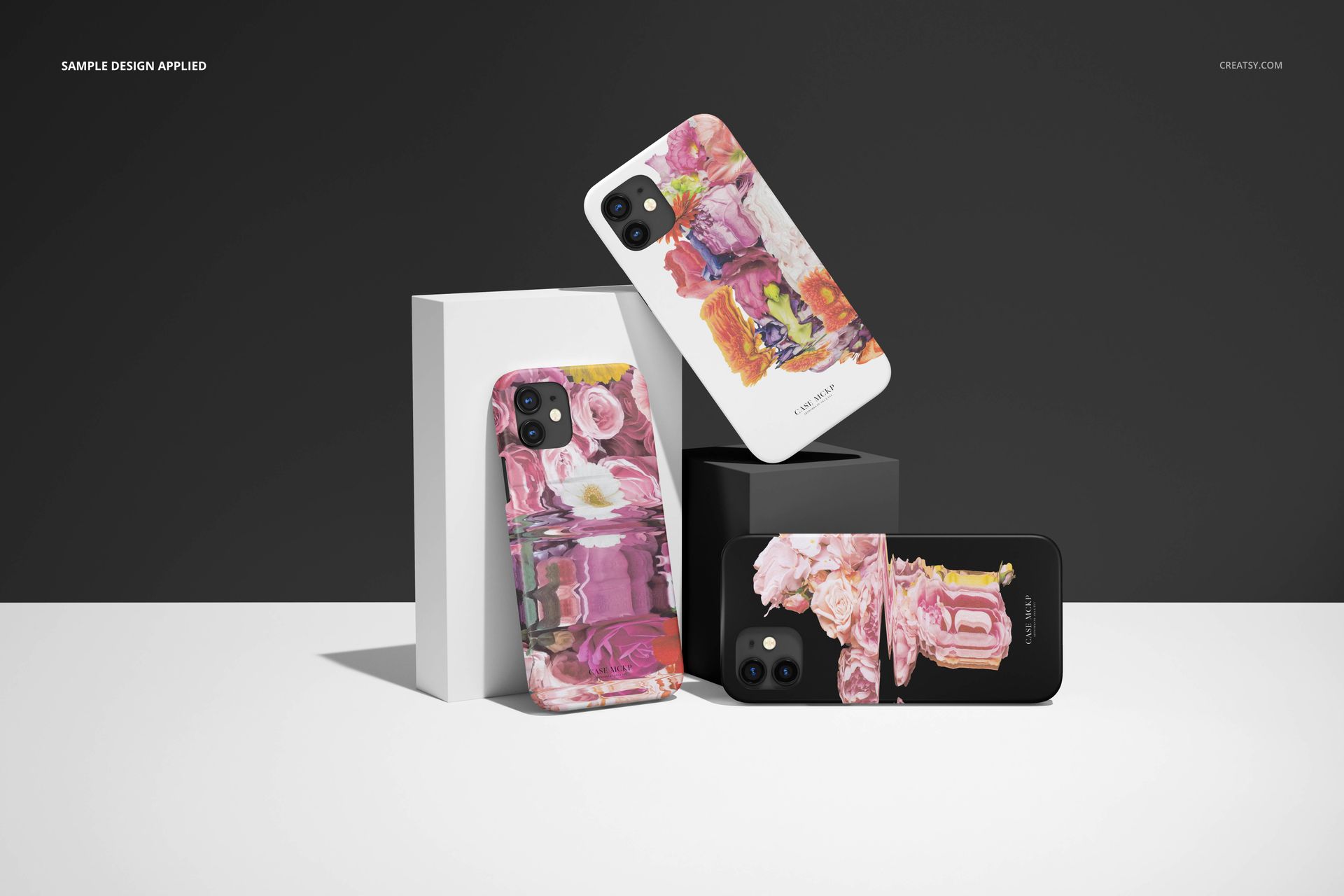 iPhone 12 matte snap case PSD mockup featuring three cases with vibrant abstract artwork, arranged on geometric blocks.